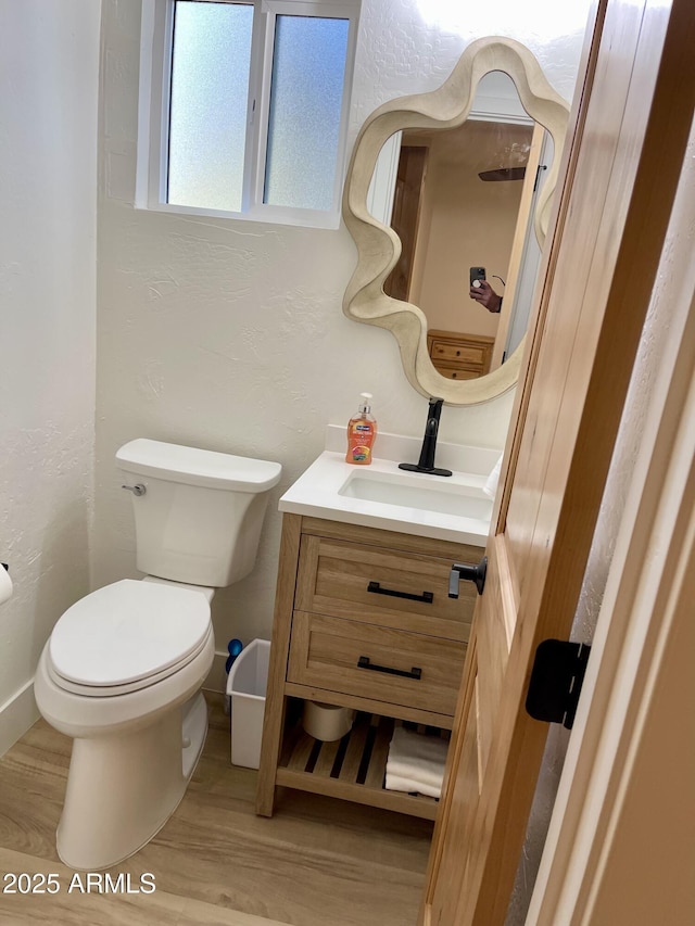 bathroom with a textured wall, vanity, toilet, and wood finished floors