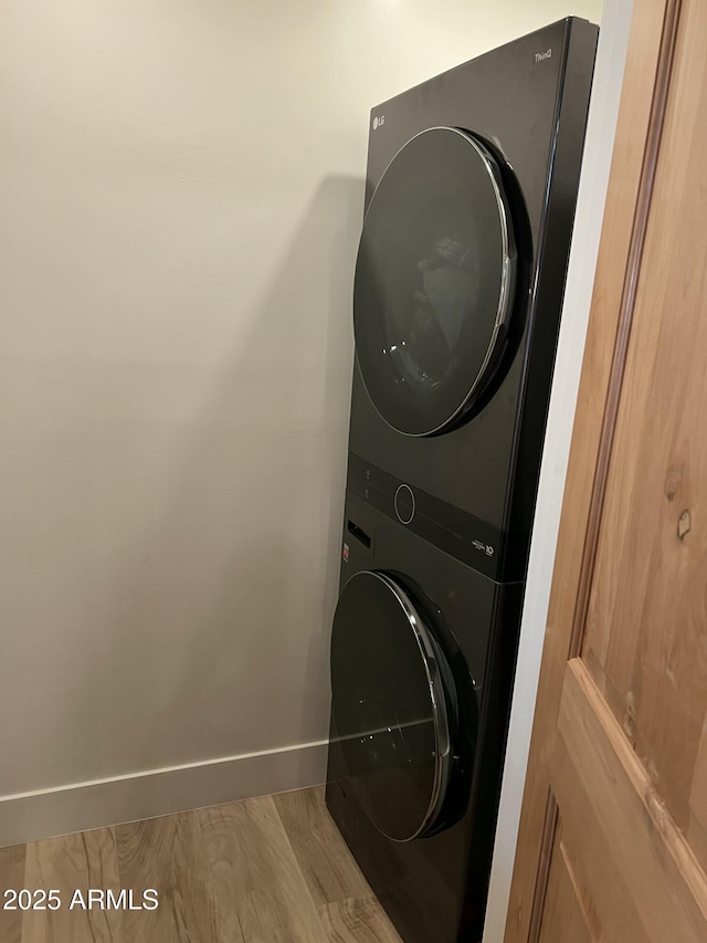 washroom with stacked washer and dryer, baseboards, laundry area, and wood finished floors