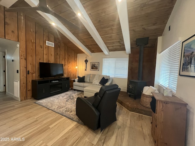 living room with a wood stove, visible vents, vaulted ceiling with beams, and light wood finished floors