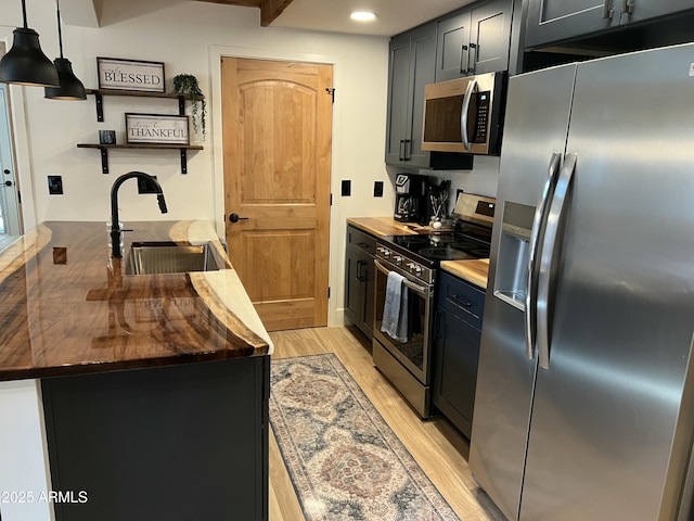 kitchen with pendant lighting, light wood finished floors, open shelves, appliances with stainless steel finishes, and a sink