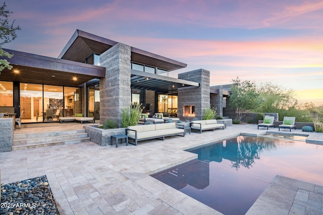 back house at dusk with an outdoor living space with a fireplace and a patio area