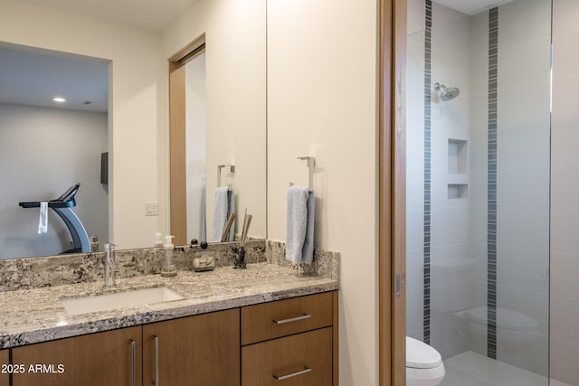 bathroom with vanity, tiled shower, and toilet