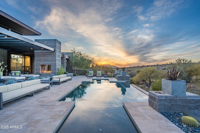 pool at dusk with an outdoor living space with a fireplace and a patio