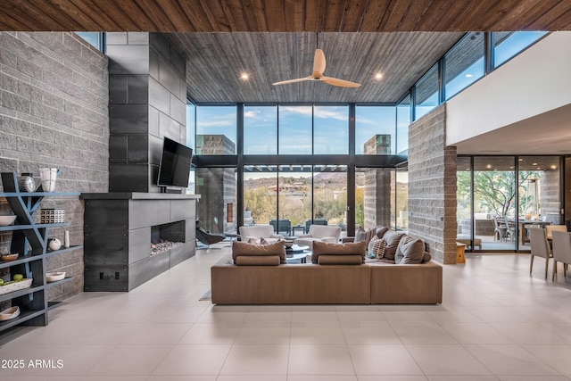 living room with floor to ceiling windows, wooden ceiling, ceiling fan, a fireplace, and a high ceiling