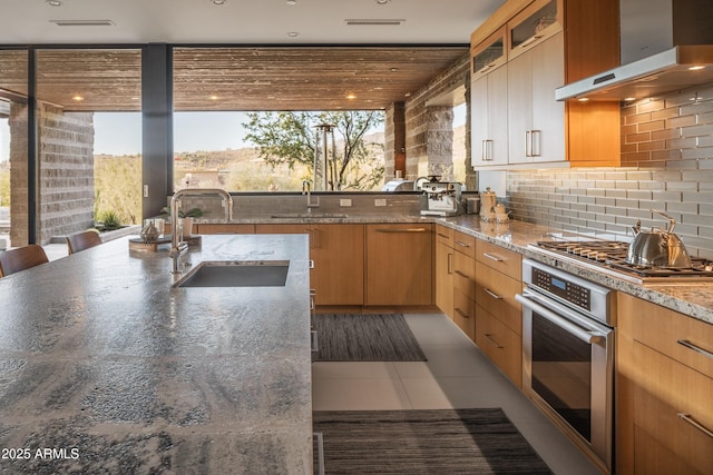 kitchen featuring tasteful backsplash, sink, light stone counters, stainless steel appliances, and wall chimney range hood