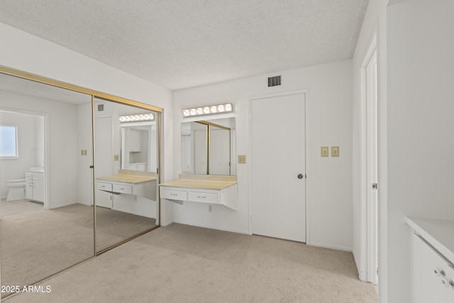 unfurnished bedroom with a textured ceiling, connected bathroom, a closet, and light carpet