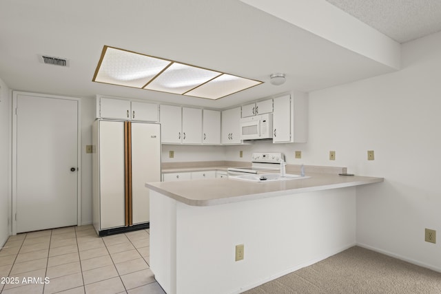 kitchen with white appliances, a peninsula, visible vents, and light countertops