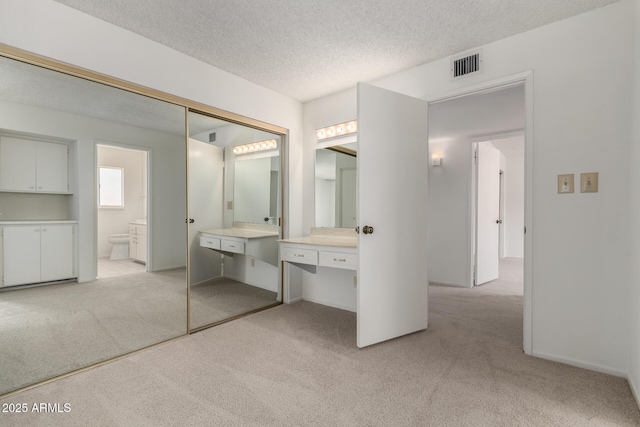 interior space with light carpet, visible vents, a textured ceiling, and ensuite bath