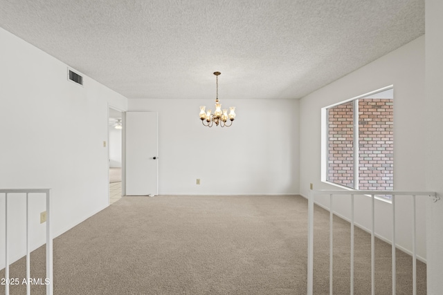 empty room with visible vents, a textured ceiling, an inviting chandelier, and carpet floors