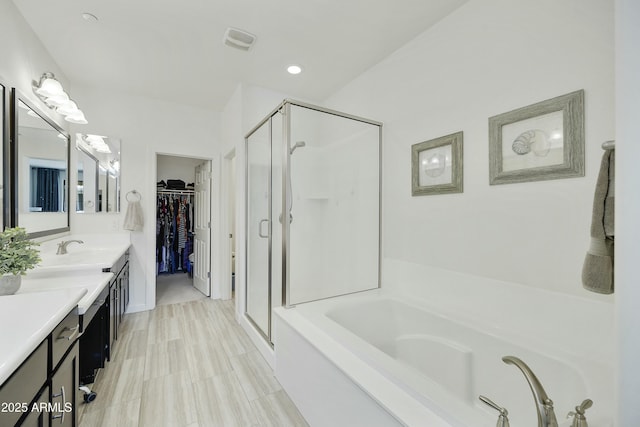 full bath featuring vanity, visible vents, a stall shower, a walk in closet, and a garden tub