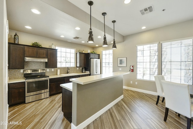 kitchen featuring visible vents, under cabinet range hood, decorative backsplash, stainless steel range with electric cooktop, and freestanding refrigerator