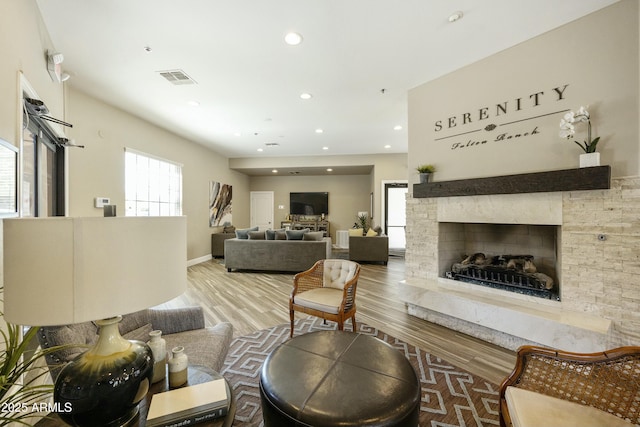 living room featuring a stone fireplace, recessed lighting, wood finished floors, and visible vents