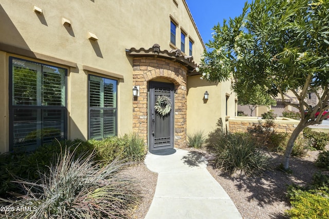 doorway to property featuring stone siding, stucco siding, and a tile roof