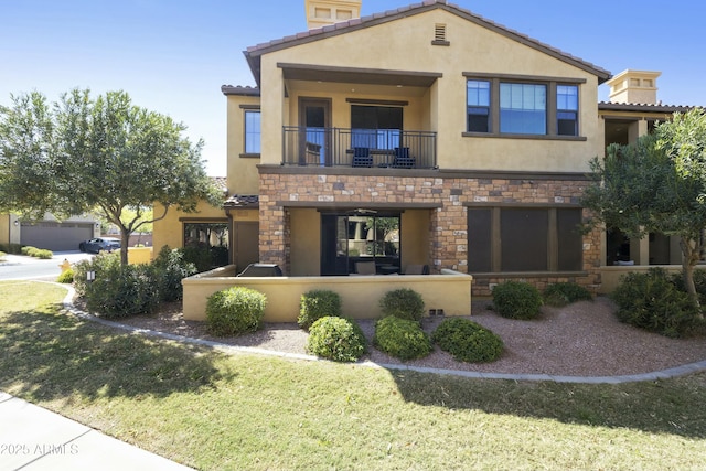 view of front of home with a front yard, a balcony, stucco siding, stone siding, and a tiled roof