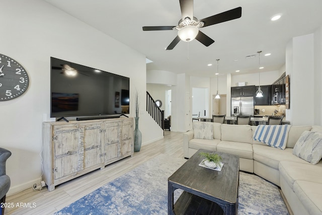 living area featuring a ceiling fan, recessed lighting, light wood-style floors, baseboards, and stairs