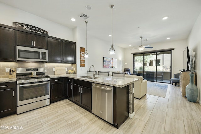 kitchen featuring visible vents, a sink, open floor plan, stainless steel appliances, and decorative backsplash