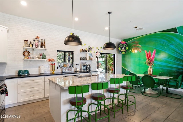 kitchen with a breakfast bar area, white cabinetry, dark stone countertops, and decorative light fixtures