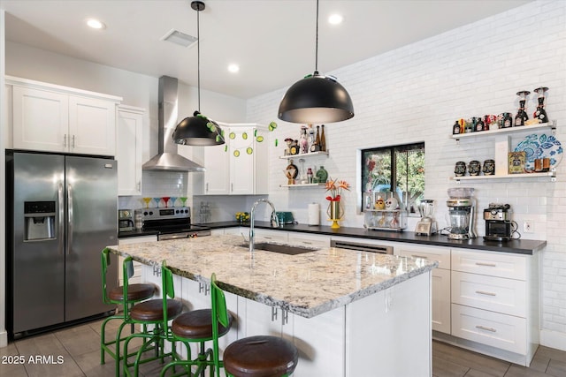 kitchen with pendant lighting, appliances with stainless steel finishes, white cabinets, wall chimney exhaust hood, and sink