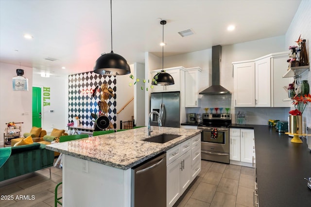 kitchen featuring white cabinetry, stainless steel appliances, decorative light fixtures, wall chimney range hood, and sink