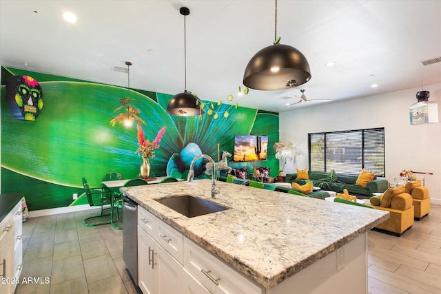 kitchen with an island with sink, white cabinets, sink, and pendant lighting