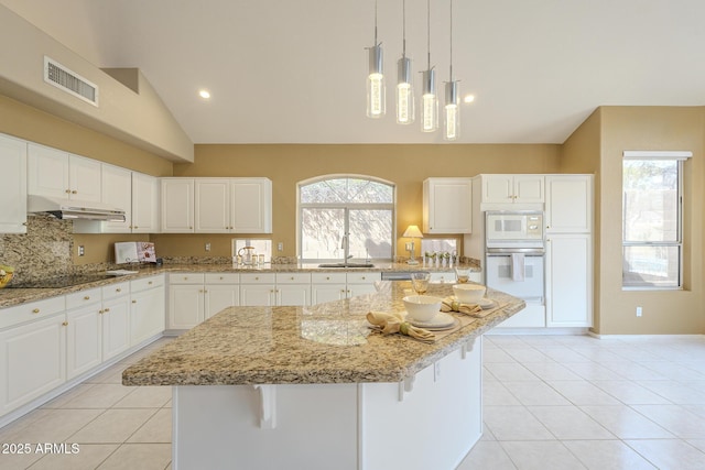 kitchen featuring light tile patterned floors, under cabinet range hood, white appliances, a sink, and visible vents