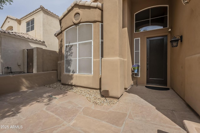 property entrance with a patio area, a tile roof, and stucco siding