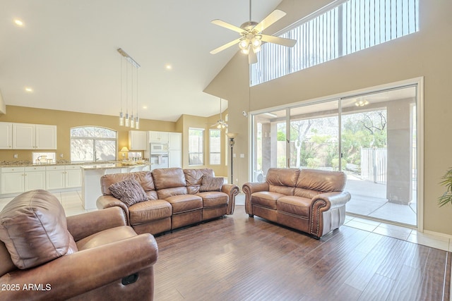 living room with light wood-style floors, recessed lighting, ceiling fan, and a high ceiling
