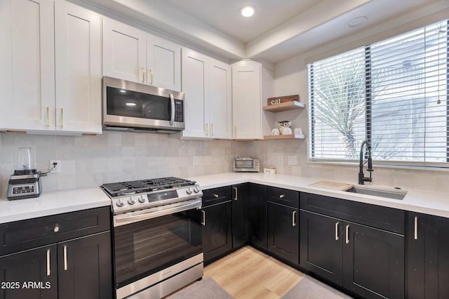 kitchen featuring sink, white cabinetry, light hardwood / wood-style flooring, stainless steel appliances, and decorative backsplash