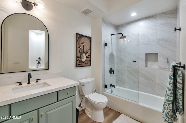 full bathroom with hardwood / wood-style flooring, tiled shower / bath, vanity, and toilet