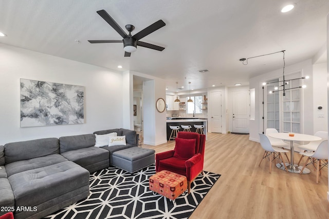 living room featuring ceiling fan with notable chandelier and light wood-type flooring