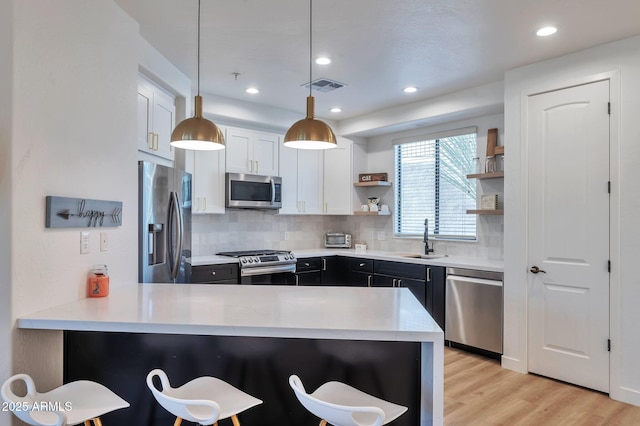 kitchen with hanging light fixtures, white cabinetry, kitchen peninsula, and stainless steel appliances