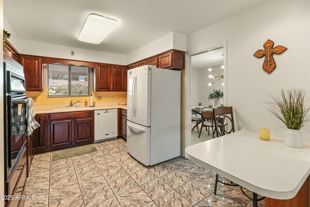 kitchen featuring white appliances, a peninsula, a sink, light countertops, and a notable chandelier