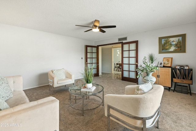 living room with ceiling fan, a textured ceiling, carpet flooring, visible vents, and baseboards