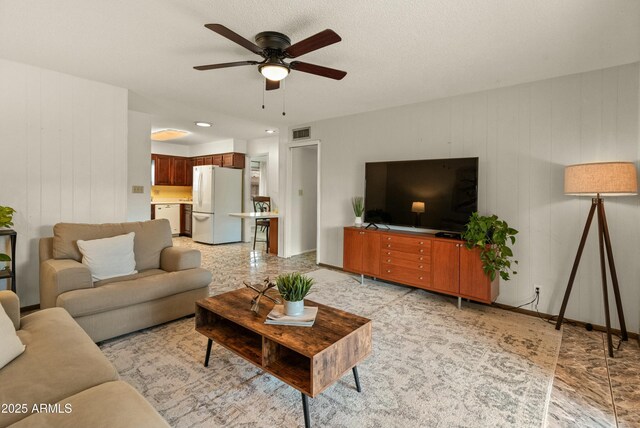 living area with a ceiling fan, visible vents, and baseboards