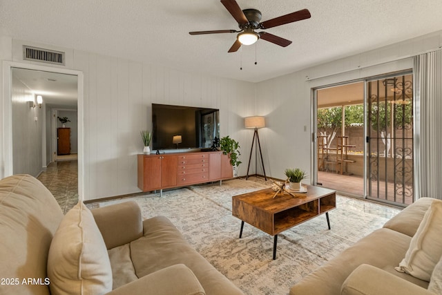 living room featuring a ceiling fan, baseboards, visible vents, and a textured ceiling