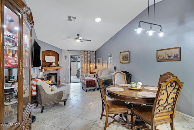 dining space with a tile fireplace, vaulted ceiling, light tile patterned flooring, and ceiling fan