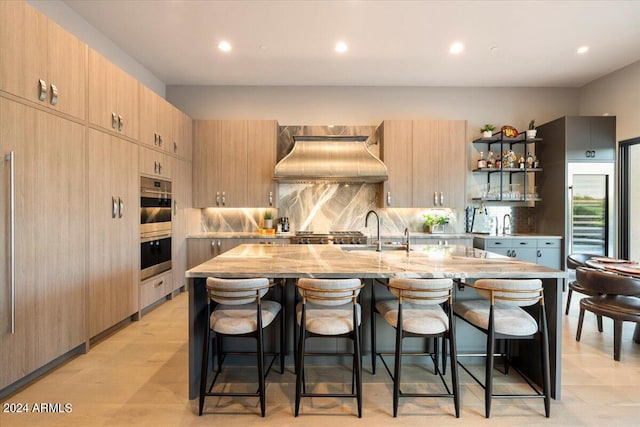 kitchen featuring an island with sink, sink, a kitchen breakfast bar, appliances with stainless steel finishes, and custom range hood