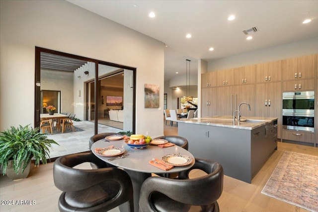 kitchen featuring an island with sink, light stone countertops, double oven, sink, and pendant lighting