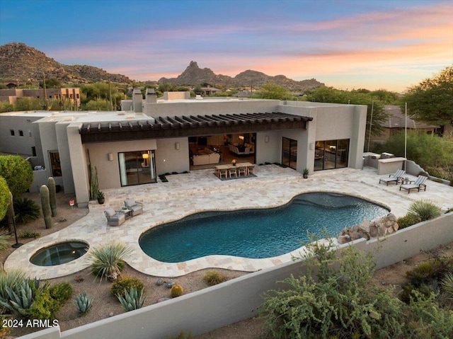 pool at dusk featuring a mountain view, an in ground hot tub, and a patio