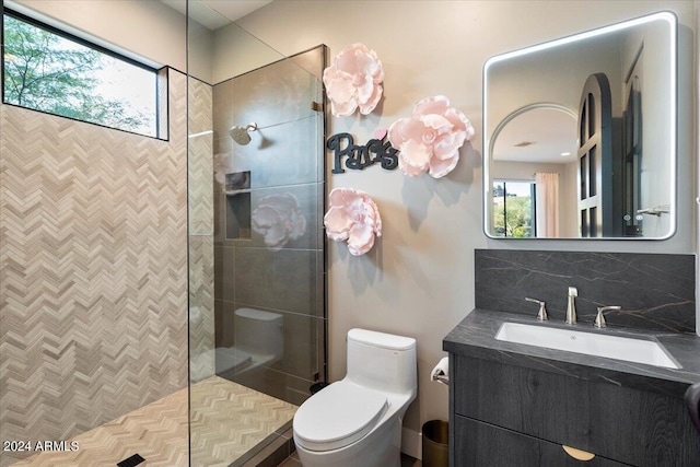 bathroom with vanity, tiled shower, toilet, and tasteful backsplash