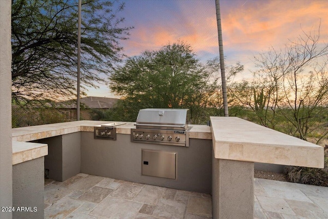 patio terrace at dusk featuring a grill and exterior kitchen