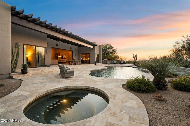 pool at dusk featuring a patio and an in ground hot tub