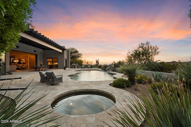 pool at dusk with an in ground hot tub and a patio