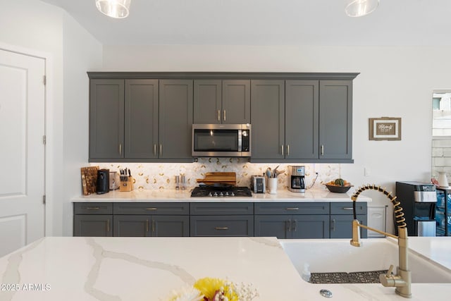 21134 W Minnezona Ave, Buckeye, AZ 85396 - kitchen with stainless steel microwave, decorative backsplash, gas cooktop, light stone counters, and gray cabinetry