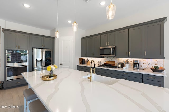 21134 W Minnezona Ave, Buckeye, AZ 85396 - kitchen with stainless steel appliances, a sink, tasteful backsplash, light stone counters, and pendant lighting