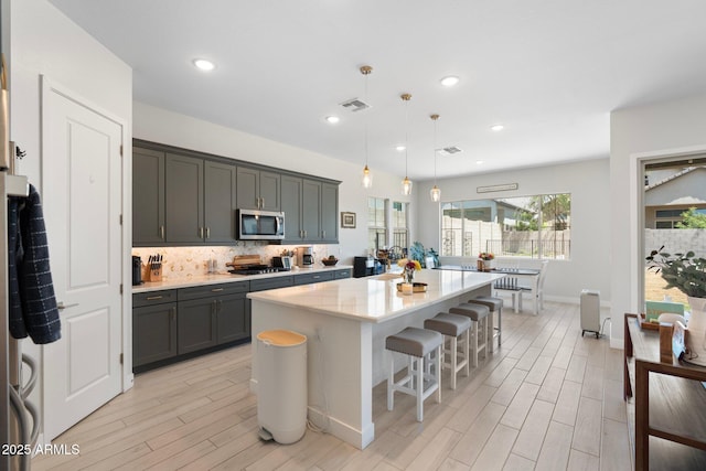 21134 W Minnezona Ave, Buckeye, AZ 85396 - kitchen featuring appliances with stainless steel finishes, light wood finished floors, a center island, tasteful backsplash, and pendant lighting
