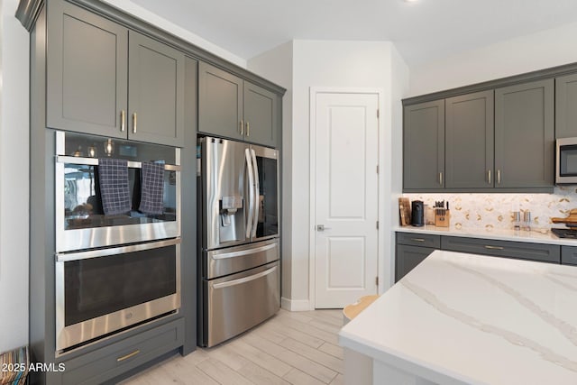 21134 W Minnezona Ave, Buckeye, AZ 85396 - kitchen featuring appliances with stainless steel finishes, backsplash, light stone countertops, light wood-style flooring, and baseboards