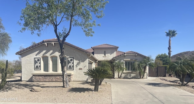 mediterranean / spanish-style home with an attached garage, driveway, a tiled roof, and stucco siding