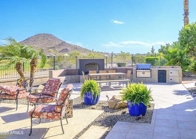 view of patio with exterior fireplace, an outdoor kitchen, a mountain view, fence, and grilling area