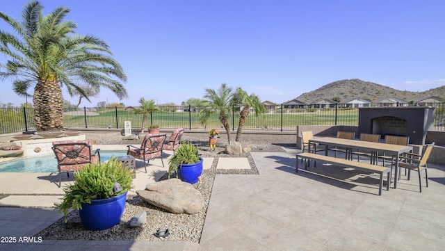 view of patio / terrace featuring outdoor dining area, an outdoor fireplace, a fenced backyard, and a mountain view